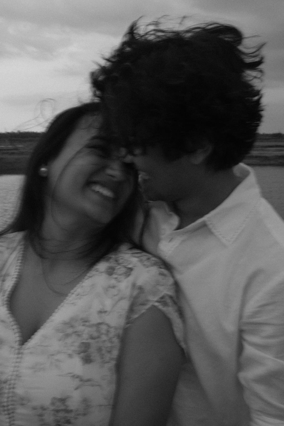 Black-and-white: a couple laughs forehead to forehead as the wind tangles their hair.