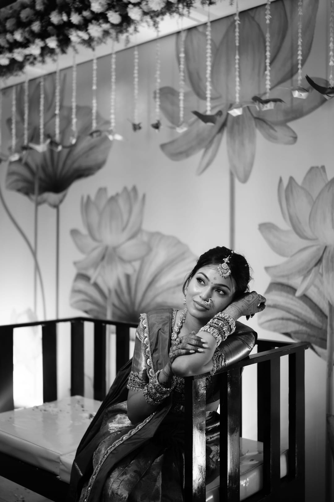 Black-and-white: the bride rests her chin on her hand and smiles, against a wall of painted lotuses.