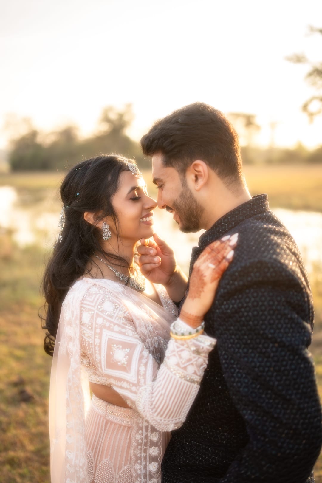 In golden backlight, a couple stands close, her hand resting on his cheek.