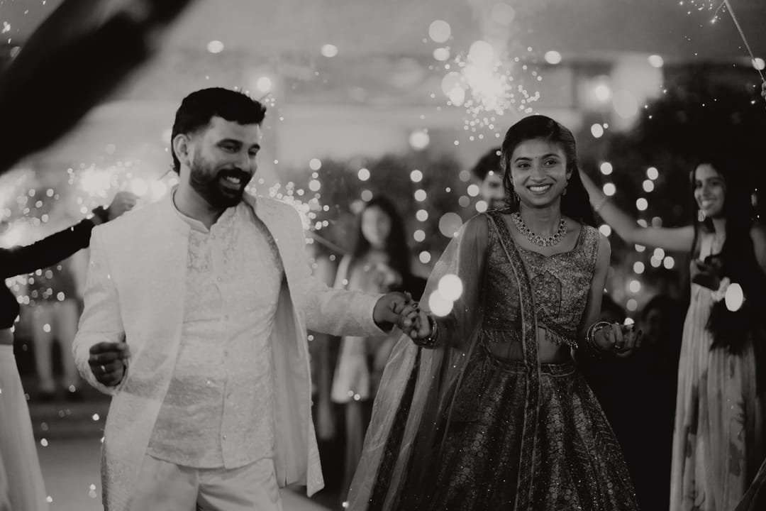Black-and-white: the couple laughs mid-dance through a tunnel of sparklers.