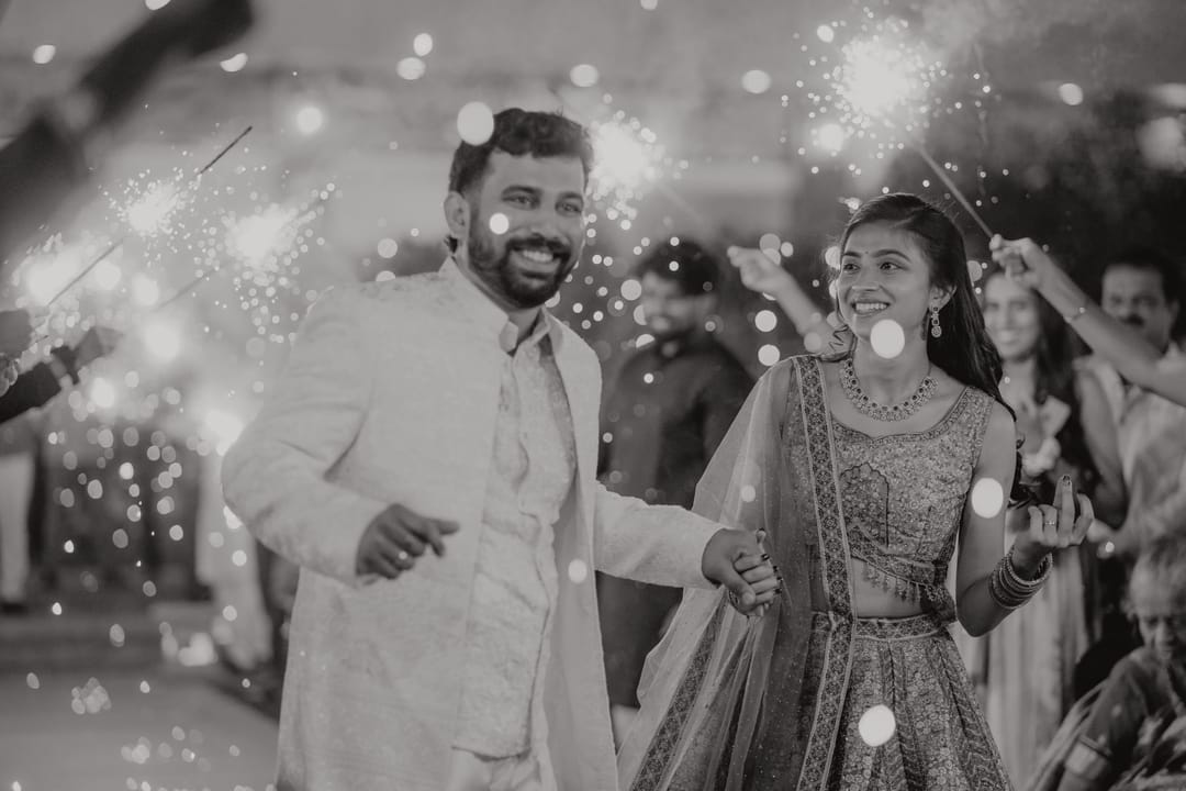 Black-and-white: the groom grins as he and the bride dance through falling sparks.