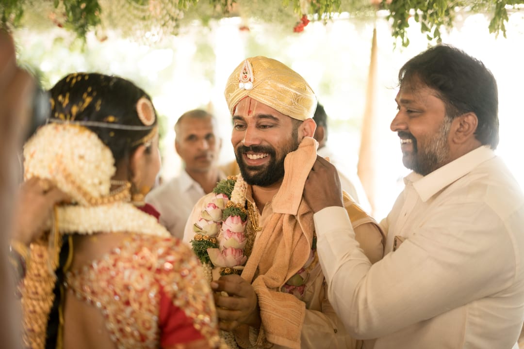 A relative playfully pinches the groom's cheeks as he laughs in his gold peta.